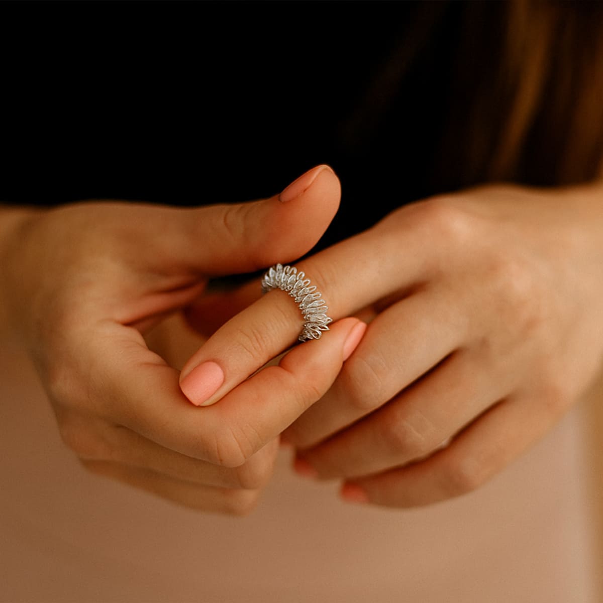 Frau massiert ihren Finger mit einem silbernen Akupressur-Ring, Nahaufnahme ihrer Hände mit gepflegten, roséfarbenen Nägeln.