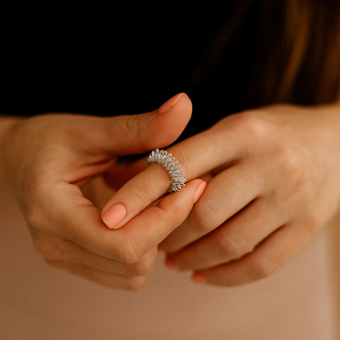 Frau massiert ihren Finger mit einem silbernen Akupressur-Ring, Nahaufnahme ihrer Hände mit gepflegten, roséfarbenen Nägeln.