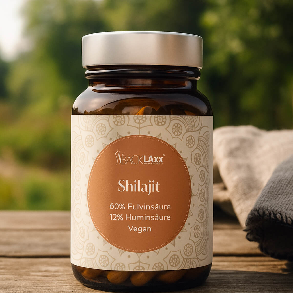 „Braunes Glas mit silbernem Deckel, darin Shilajit-Kapseln von BACKLAXX. Auf dem Etikett stehen 60 % Fulvinsäure, 12 % Huminsäure und Vegan. Die Flasche steht auf einem Holztisch, im Hintergrund Natur und Stofftuch.