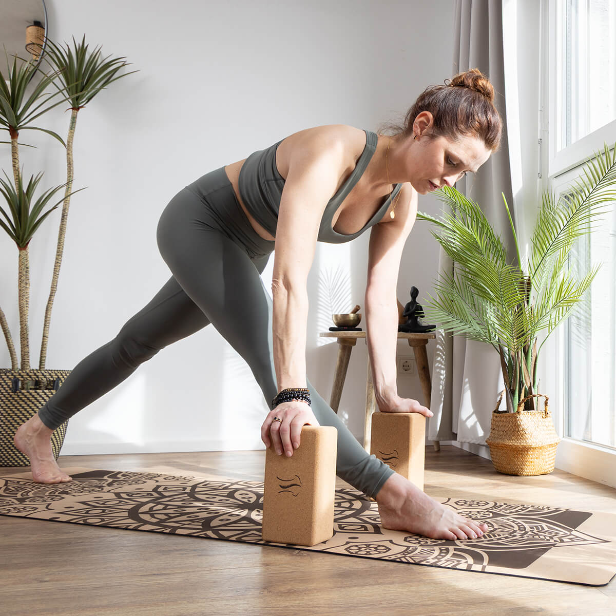 BACKLAXX Yoga-Blöcke unterstützen fortgeschrittene Dehnungsposition - Frau in grauer Sportkleidung nutzt Korkblöcke für Stabilität in hellem Yoga-Raum
