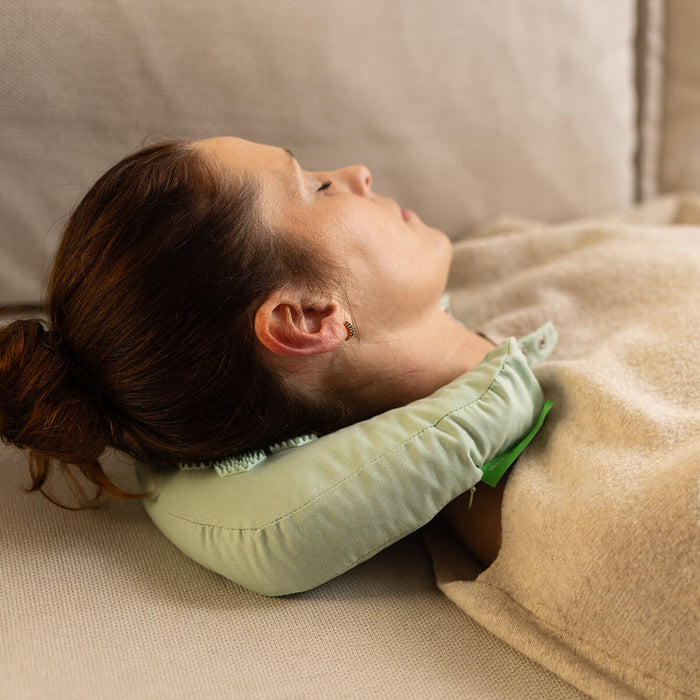 Frau entspannt mit hellgrünem U-förmigen Nackenstützkissen auf beiger Decke - Gemütliche Ruhepause mit komfortabler Nackenunterstützung
