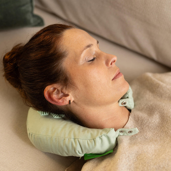 Frau entspannt mit hellgrünem Nackenkissen auf Sofa - Komfortables Schlaf- und Reisekissen für erholsame Ruhezeiten unter beiger Decke
