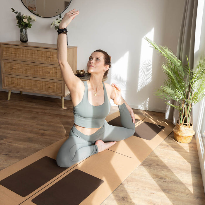 Frau praktiziert Yoga im hellen Wohnraum - Entspannte Asana auf gemusterter Matte mit Zimmerpflanzen für Achtsamkeit und Balance