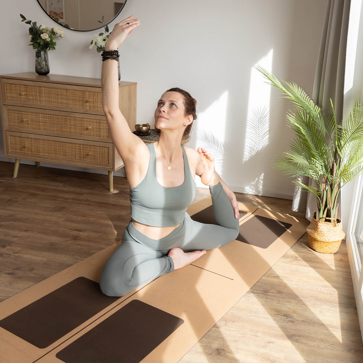 Frau praktiziert Yoga im hellen Wohnraum - Entspannte Asana auf gemusterter Matte mit Zimmerpflanzen für Achtsamkeit und Balance